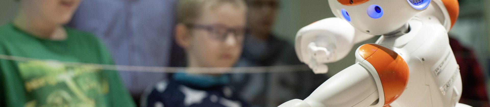 Kinder beobachten einen kleinen Roboter, der sich im Bildvordergrund befindet.