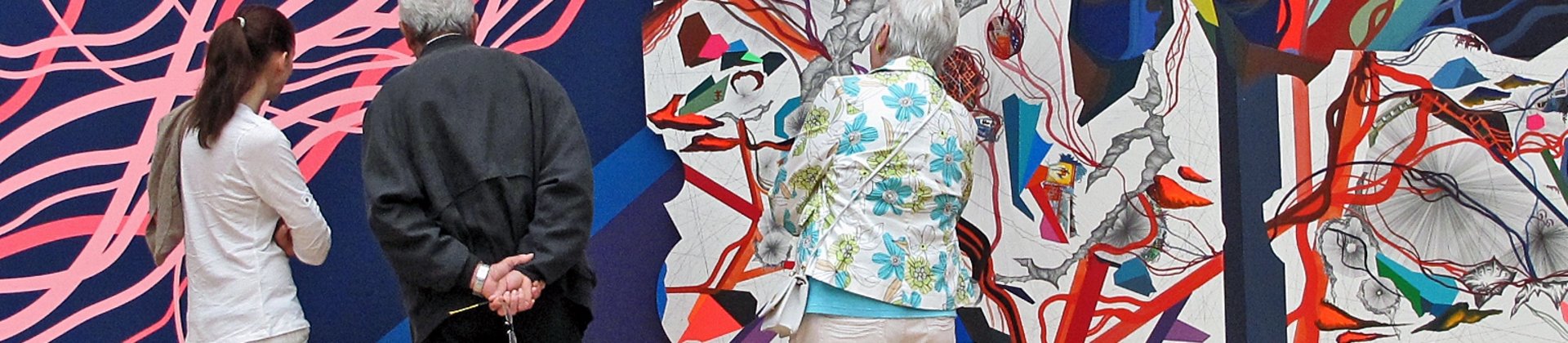 Drei Personen betrachten eine bunte Ausstellungswand.